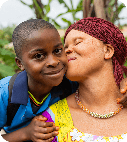 Smiling boy in school uniform with his mother kissing his cheek.